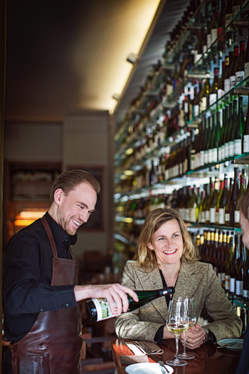 Vinothek mit zwei Personen. Es wird Wein eingeschenkt. fröhliche Stimmung
